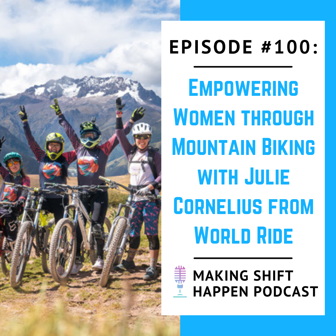 A group of four female mountain bikers in helmets and multi-colored long sleeve World Ride jerseys stand next to their bikes on top of a yellow grassy knoll in front of a white snow-capped mountain in Peru. They all have their hands up in the air in celebration.