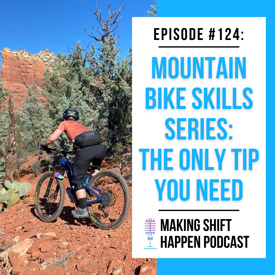 Jen is wearing black shorts, black knee pads, and a corral jersey as she bikes up a switch back in Sedona with the red rocks in the background.