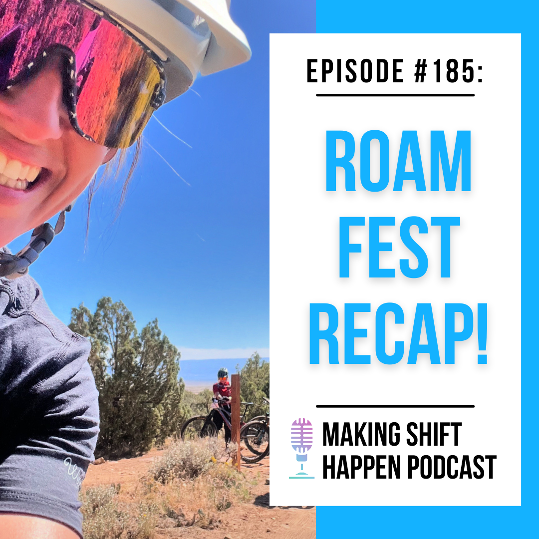 Jen is wearing a white helmet and a grey Wild Rye t-shirt, and is smiling as she is looking into the camera with another mountain biker behind her standing on their bike in the Fruita desert.